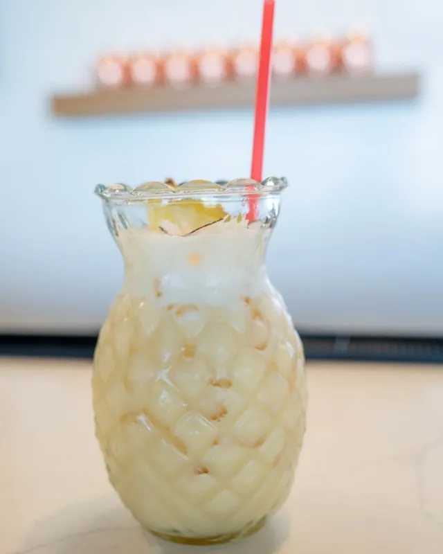 Frozen piña colada in a textured pineapple glass with a red straw