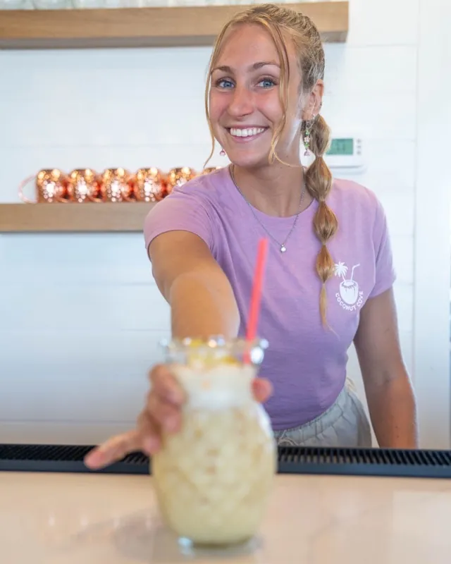 A bartender sliding a piña colada across the marble bar top