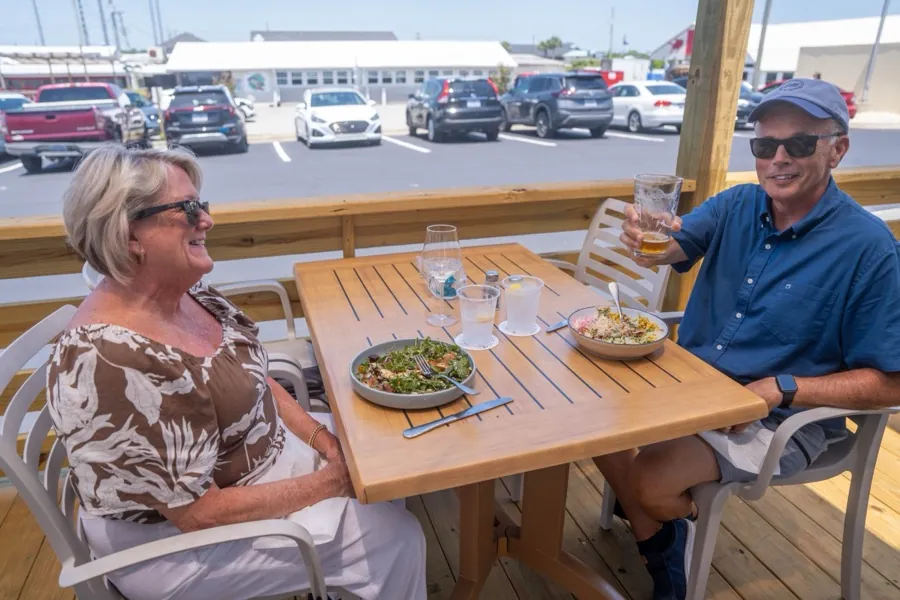 Guests eating lunch at a table on the covered deck, looking out toward the lot and waterway